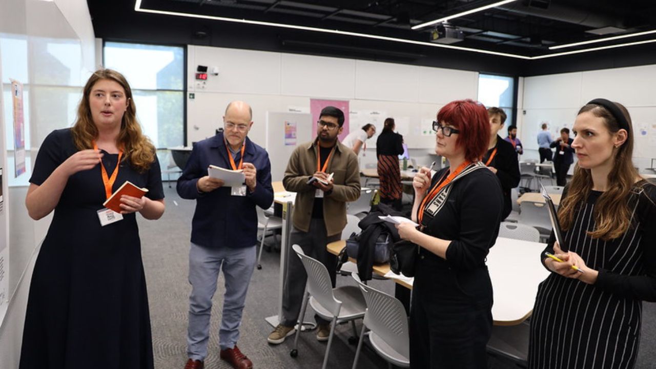 2025 Social Services Researchers standing listening to ADM+S student present research poster